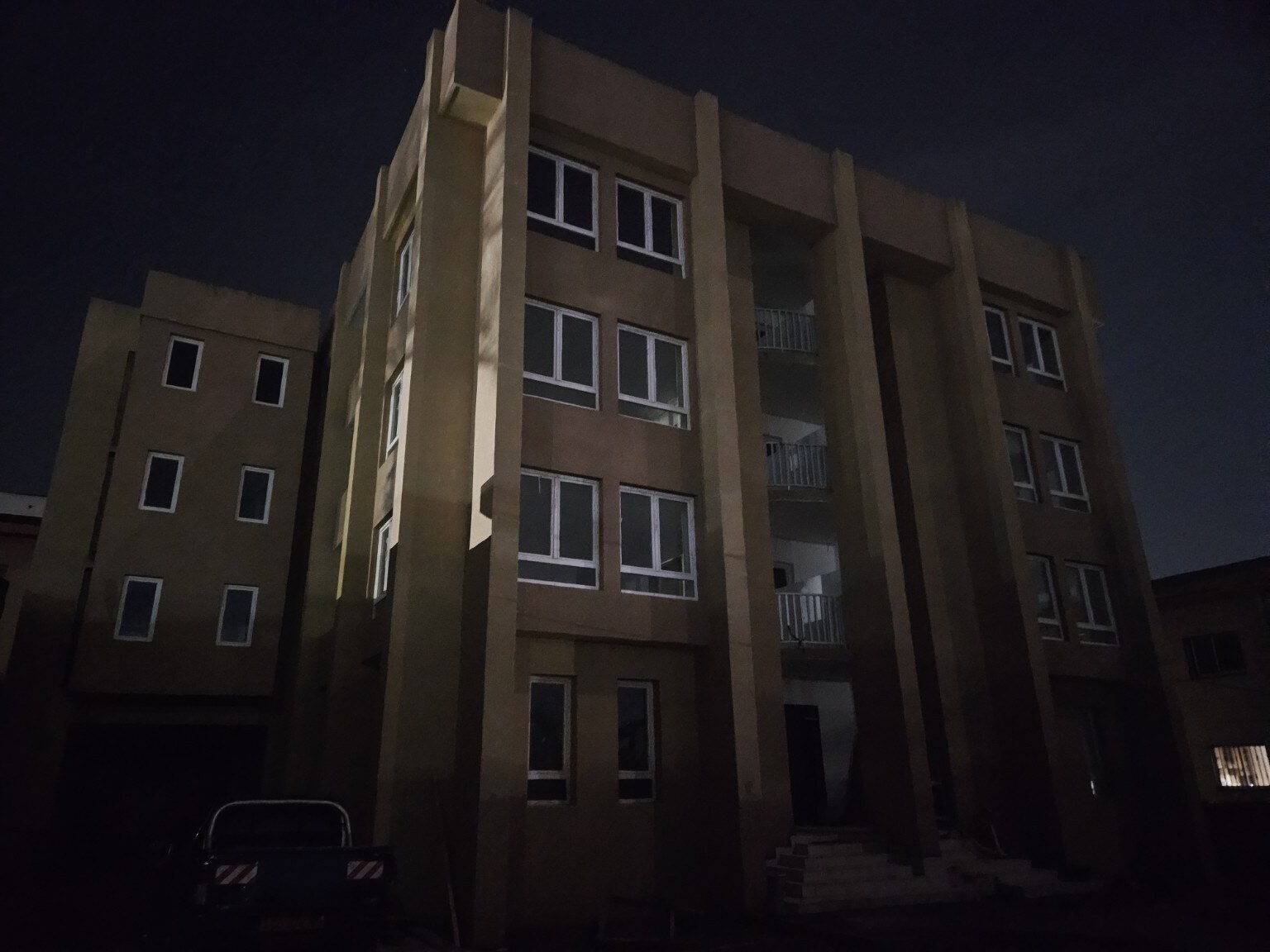 Golf Residences at night during final construction work, showing the completed massing, vertical façade elements, windows, and recessed balconies.